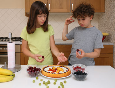 Kids putting fruit on cake